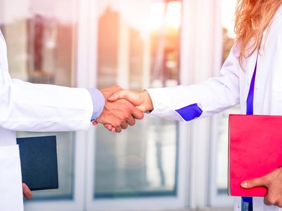 Two people in lab coats shaking hands